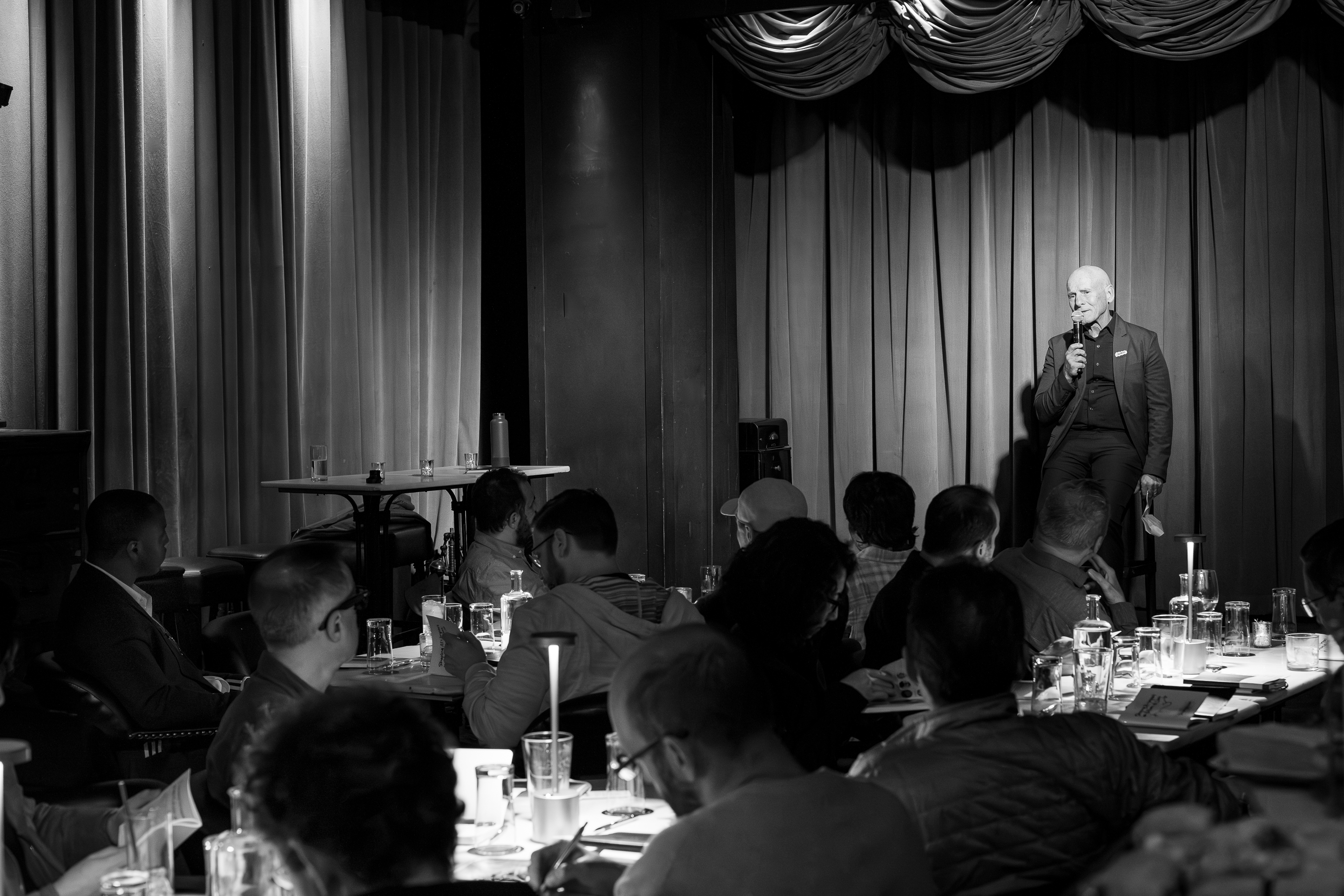 A black and white photo of a Dave Patterson on stage kicking off the Salon