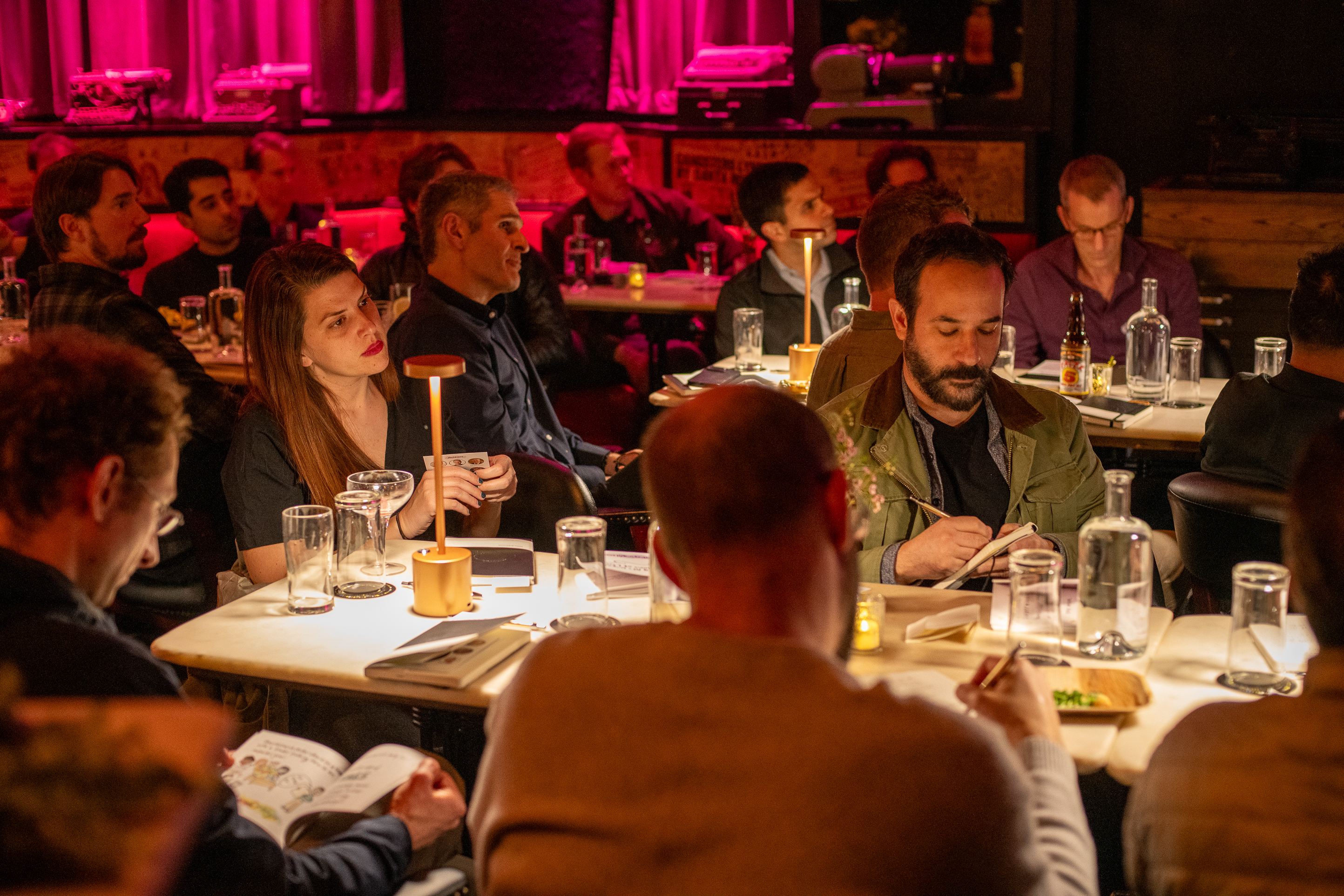 A warmly lit photo of attendees at tables during a salon event